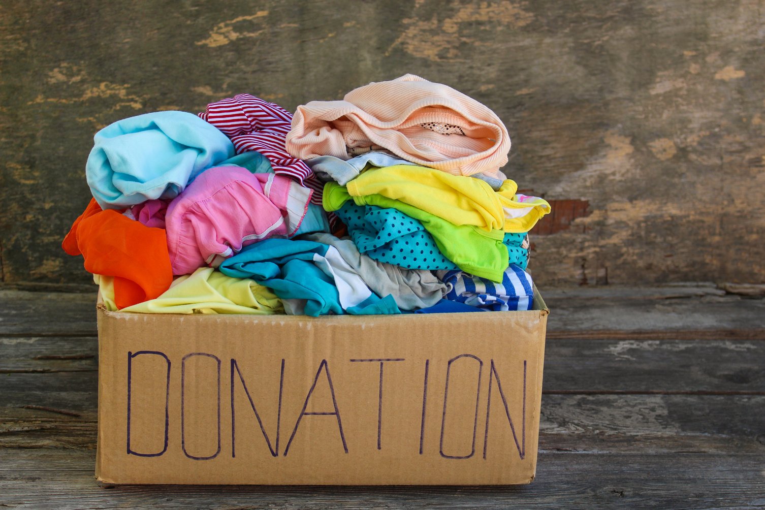 Donation box with clothes on the old wooden background.